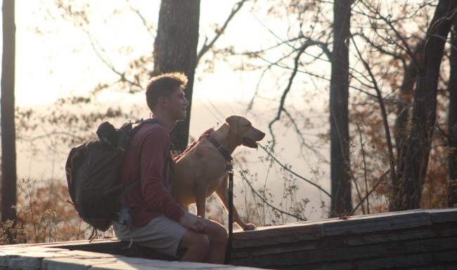 We welcome your pet family a man with a backpack sitting on a log with a dog
